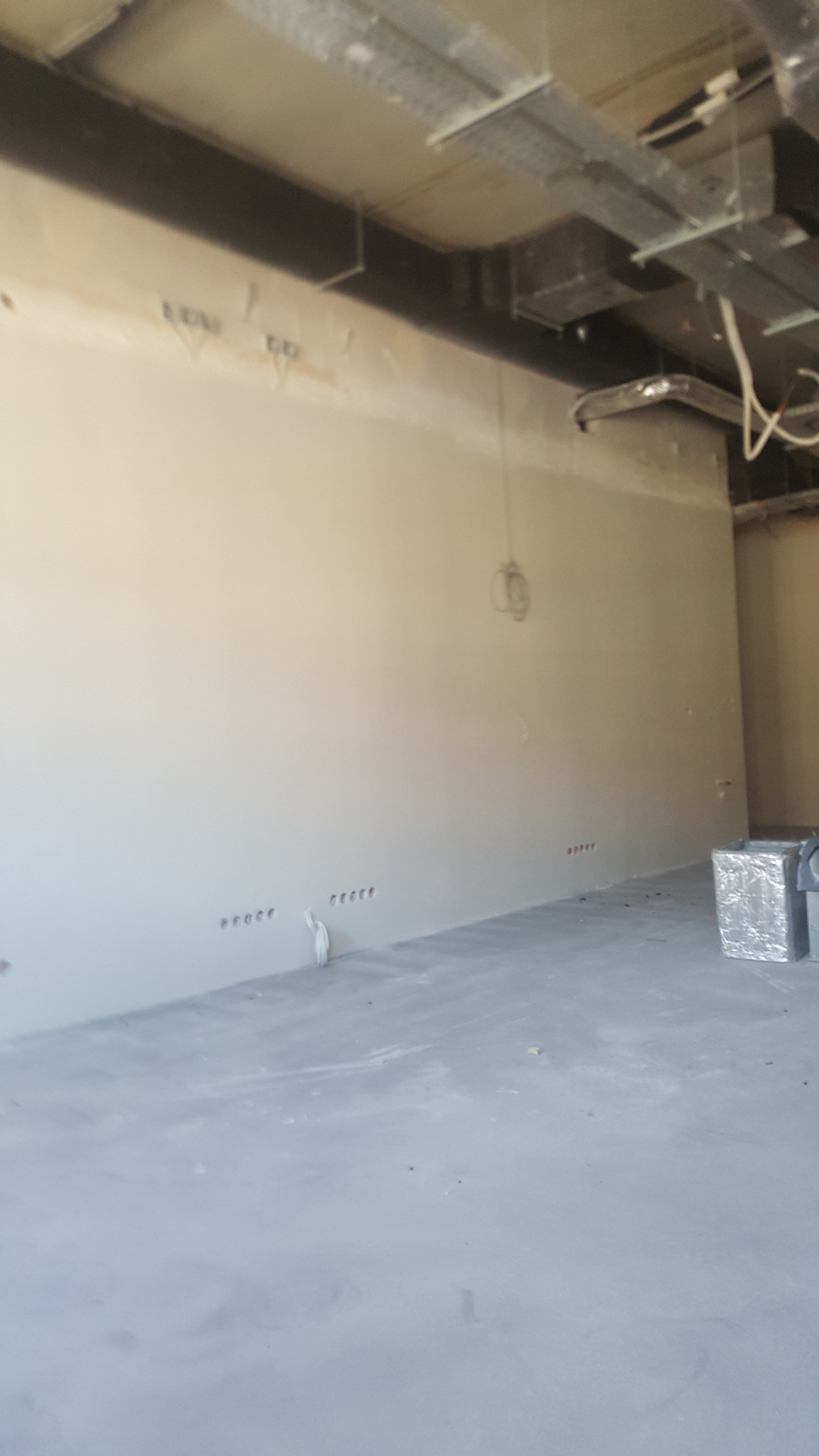 Wnętrze w trakcie wykańczania: ściana po wstępnym wyrównaniu z widocznymi otworami na instalacje elektryczne, sufit z instalacjami, przygotowany do dalszych prac. Na podłodze widoczne ślady po...