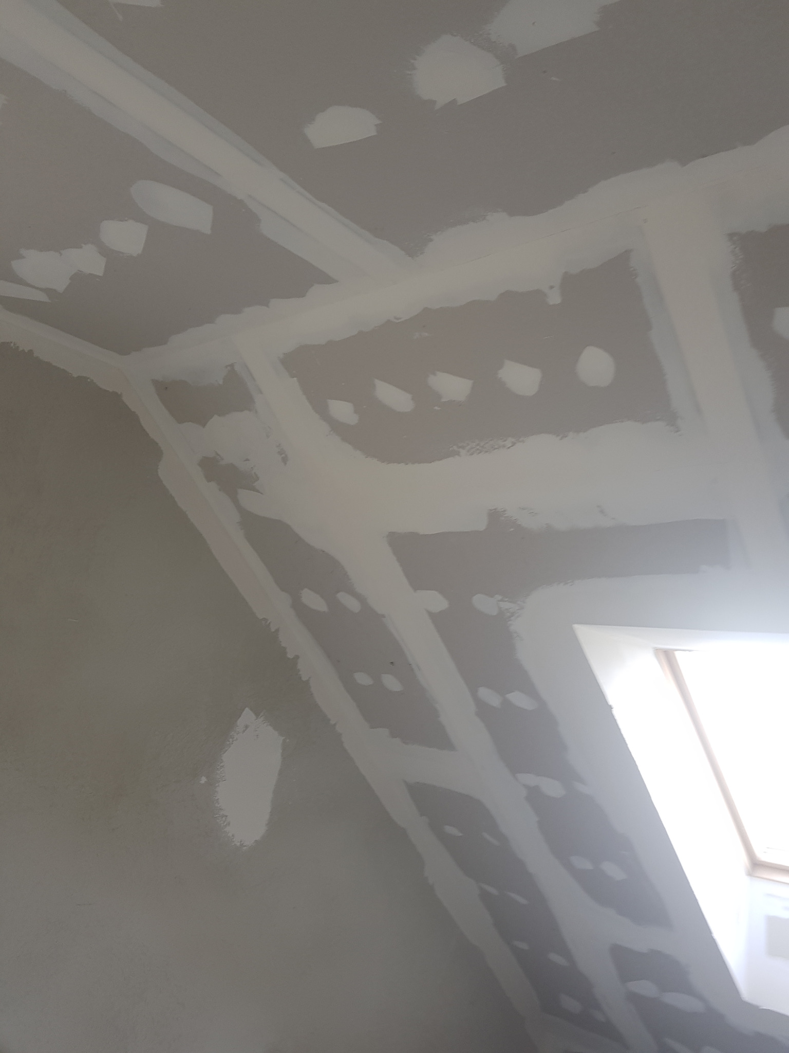 Ściana poddasza w trakcie prac wykończeniowych, widoczne nałożone warstwy wyrównujące z niedoskonałościami, przygotowane pod dalsze prace wykończeniowe.