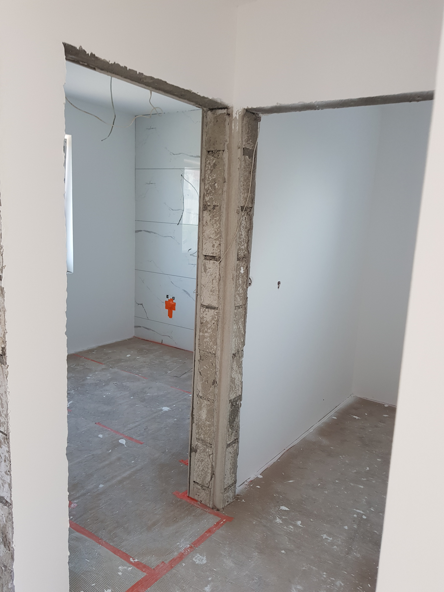 Przygotowanie do malowania: surowe ściany z widocznymi śladami po szpachlowaniu i zaznaczonymi liniami na podłodze, widok przez dwa surowe otwory drzwiowe.