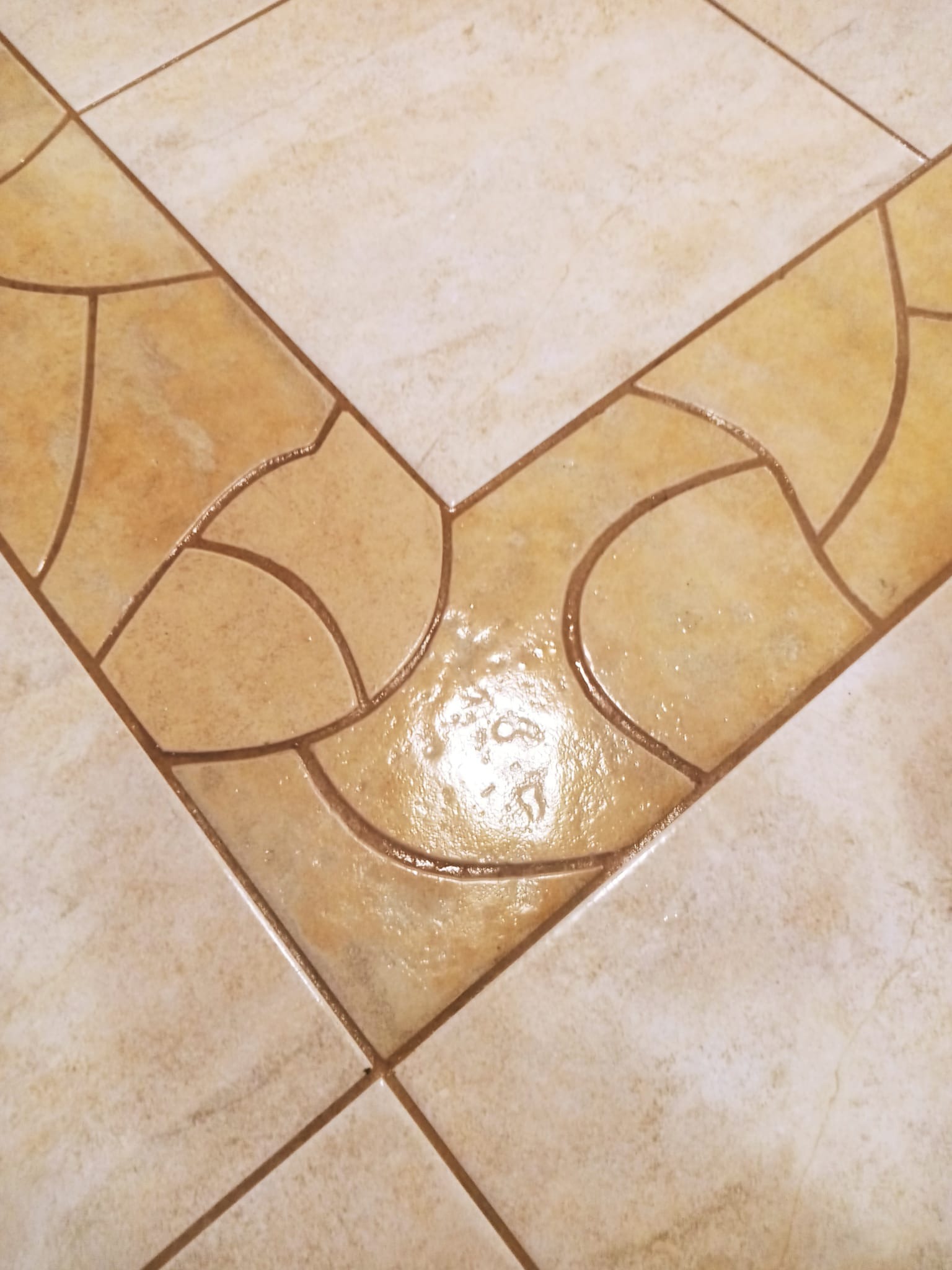 Fragment podłogi z jasnobeżowych płytek ceramicznych ułożonych w geometryczny wzór, z widocznymi smugami po niedawnym umyciu.