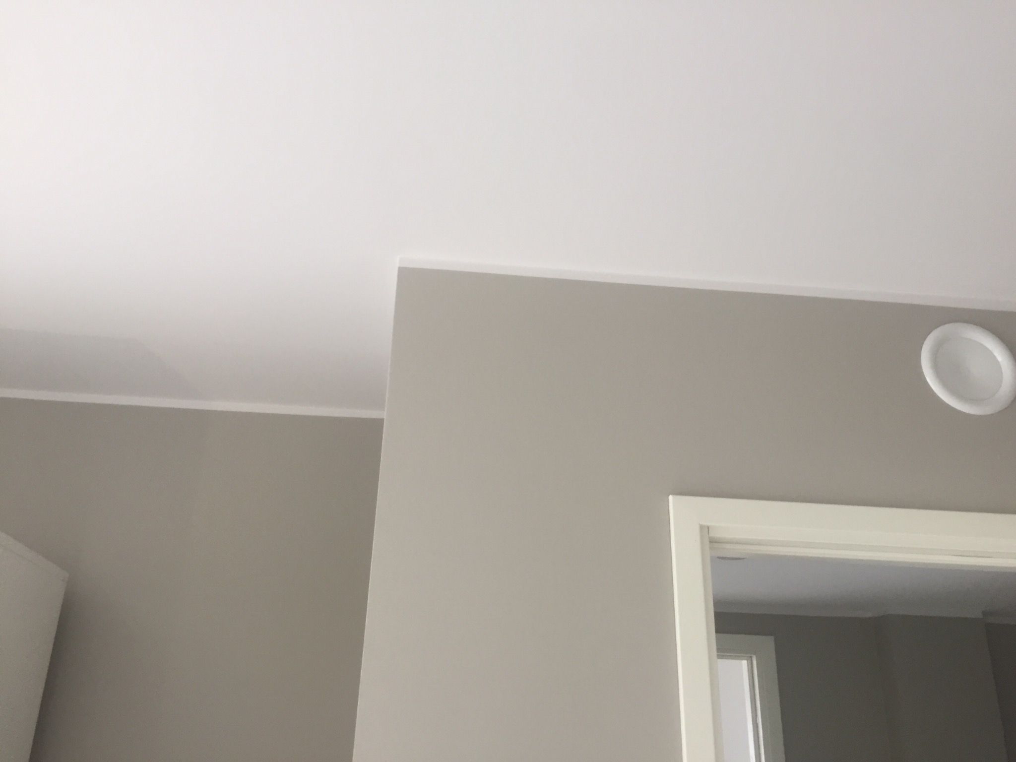 Fragment wnętrza po odświeżeniu: świeżo pomalowane ściany w odcieniach szarości, biały sufit z delikatną listwą oraz widoczny fragment białej ościeżnicy drzwiowej i okrągły nawiewnik sufitowy.