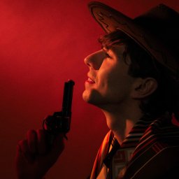 Natalia Mazurkiewicz-Szafarska - Mężczyzna w kapeluszu kowbojskim, z rewolwerem, w dramatycznym, czerwonym oświetleniu, profil. Ujęcie stylizowane na film noir.