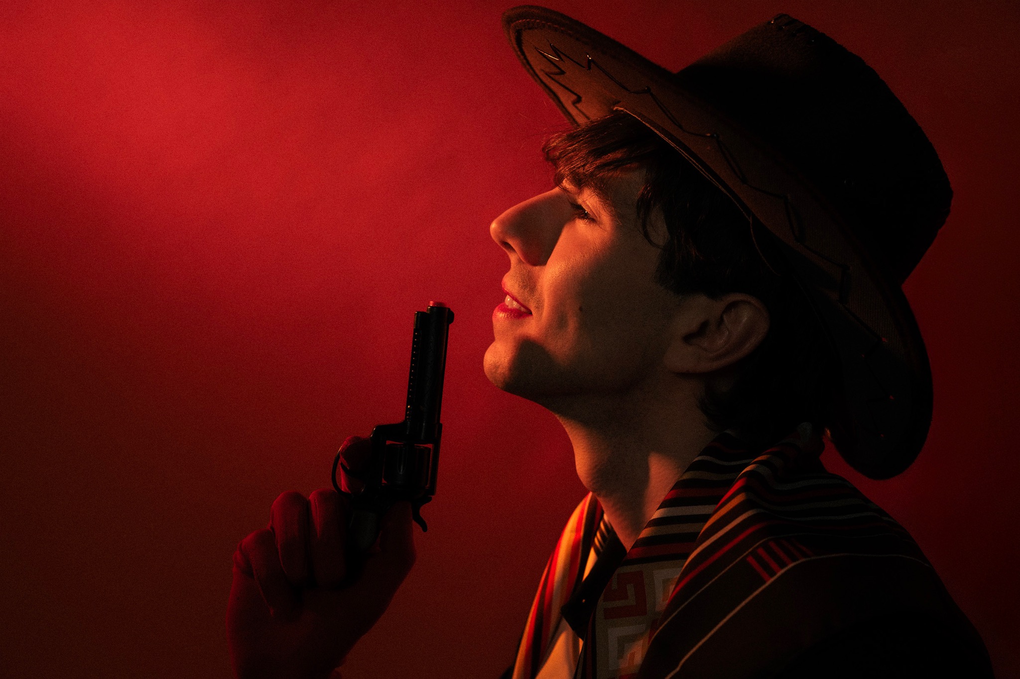 Mężczyzna w kapeluszu kowbojskim, z rewolwerem, w dramatycznym, czerwonym oświetleniu, profil. Ujęcie stylizowane na film noir.