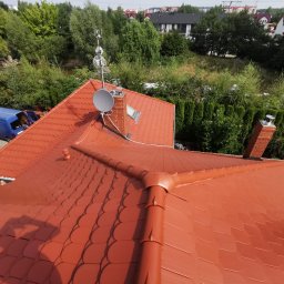 Dach-bud Dariusz matecki - Czerwony dach z dachówki bitumicznej widziany z góry, z anteną satelitarną, kominem i niebieskim samochodem dostawczym w tle.