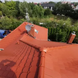 Czerwony dach z dachówki bitumicznej widziany z góry, z anteną satelitarną, kominem i niebieskim samochodem dostawczym w tle.