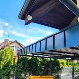 Dach-bud Dariusz matecki - Nowoczesna wiata z metalową konstrukcją i obróbkami blacharskimi w kolorze grafitowym, widoczna maszyna do obróbki blachy Sorex na tle zadbanego ogrodu.