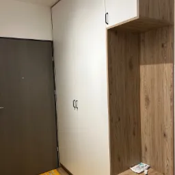 Nowoczesna szafa wnękowa z białymi frontami i drewnopodobnym regałem, widoczne akcesoria i resztki po montażu na blacie