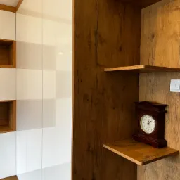 Nowoczesna zabudowa z drewnianymi akcentami: białe szafki z kwadratowymi wnękami i drewniane półki z dekoracyjnym zegarem.