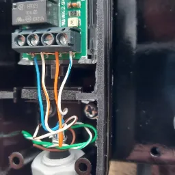 Wnętrze obudowy sterownika z widoczną płytką drukowaną, złączami śrubowymi i podłączonymi przewodami o różnych kolorach: niebieskim, białym, pomarańczowym i zielonym, skierowanymi w dół...