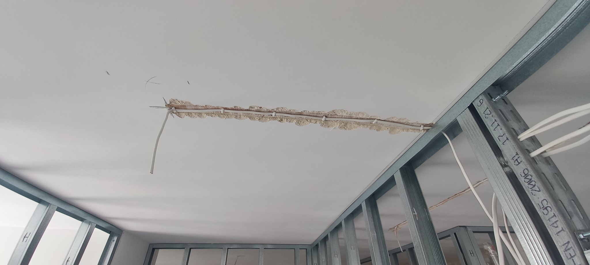 Przewody elektryczne prowadzone w bruździe w suficie podwieszanym, widoczne metalowe profile konstrukcyjne.