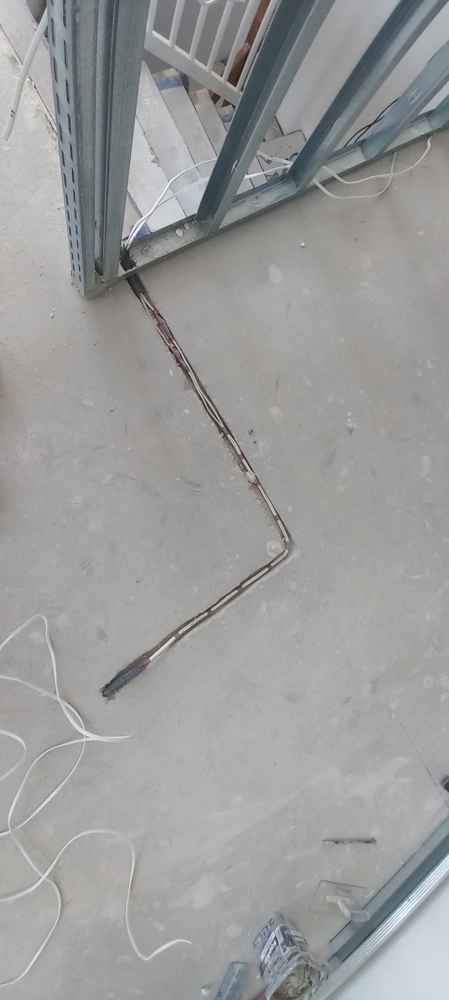 Wykopany w szarej posadzce kanał z ułożonym kablem elektrycznym, widoczne metalowe profile konstrukcyjne.