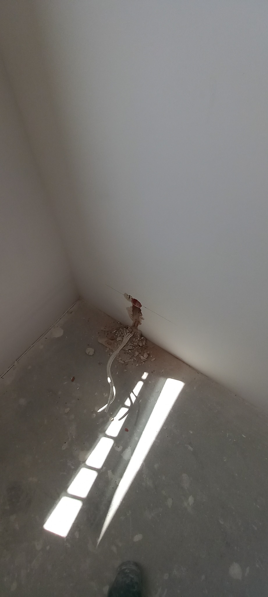 Przygotowanie do instalacji elektrycznej w Pisarzowicach: przewody wystające ze ściany, otoczone gruzem po kuciu, w surowym wnętrzu z betonową podłogą.