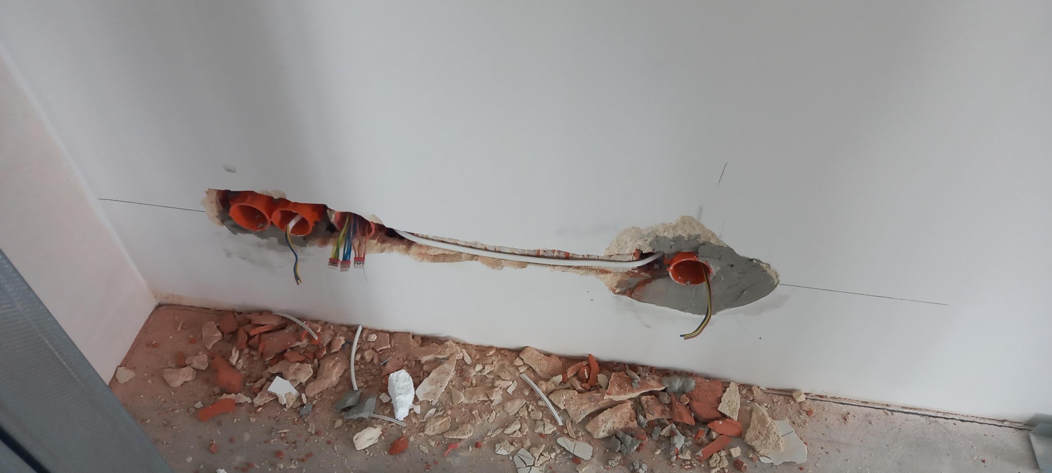 Wykute bruzdy w suficie z widocznymi pomarańczowymi puszkami instalacyjnymi i przewodami elektrycznymi, gruz na podłodze.