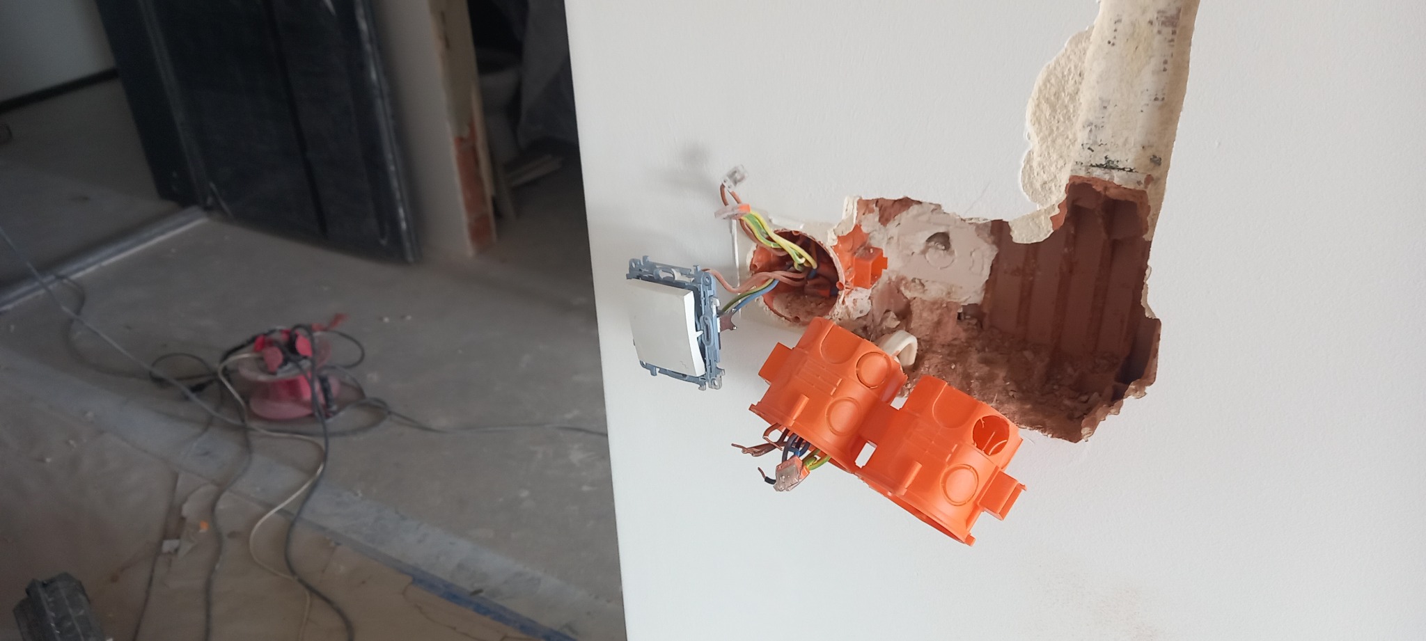 Przygotowanie do montażu włącznika światła: puszki instalacyjne częściowo osadzone w ścianie, widoczne przewody elektryczne i kabel na podłodze w trakcie remontu.