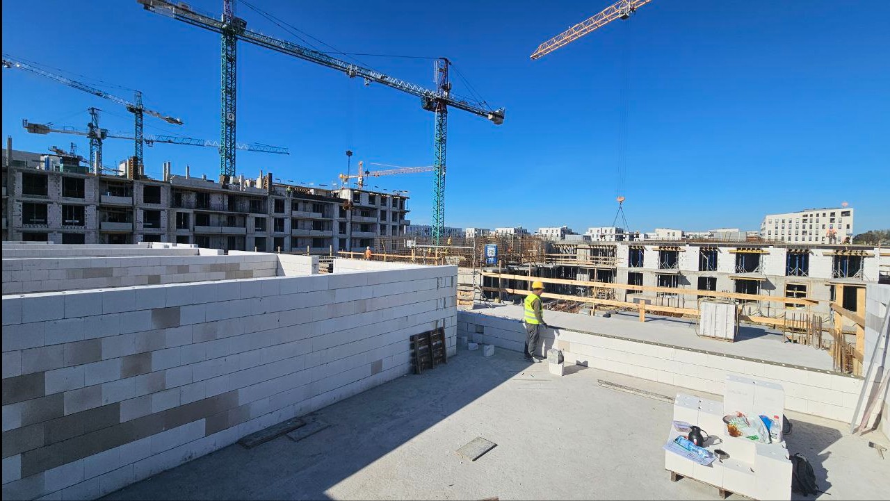Budowa wielopiętrowego budynku z betonu komórkowego. Na pierwszym planie ściany, w tle żurawie i kolejne budynki w stanie surowym.