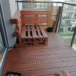 Drewniany, surowy mebel z palet, prawdopodobnie sofa, na balkonie w Słubicach. Widoczne deski podłogowe i fragmenty elewacji budynku.