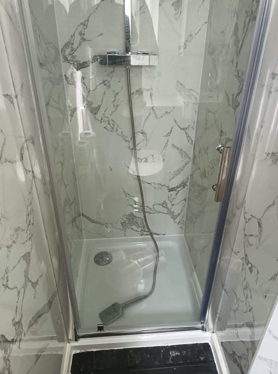 Kabina prysznicowa z brodzikiem i chromowaną armaturą, wykończona panelami ściennymi imitującymi marmur, widoczna szpachelka na dnie brodzika.