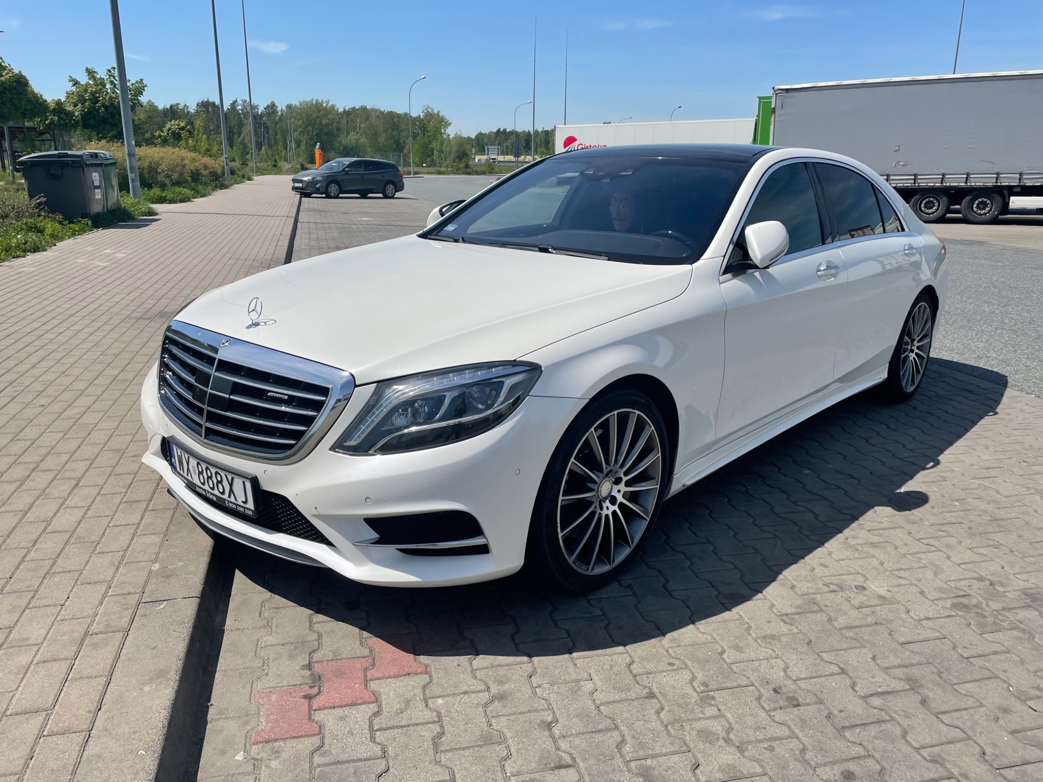 Biały Mercedes-Benz S-Class z czarnym dachem panoramicznym, zaparkowany na parkingu z kostki brukowej, z widoczną tablicą rejestracyjną i przyciemnionymi szybami.