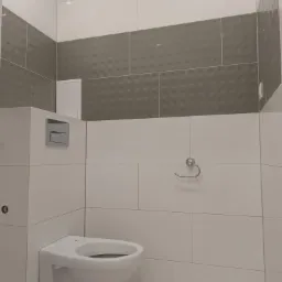 Nowoczesna toaleta podwieszana w łazience z białymi i szarymi płytkami, widoczny przycisk spłuczki, uchwyt na papier toaletowy i kratka wentylacyjna.