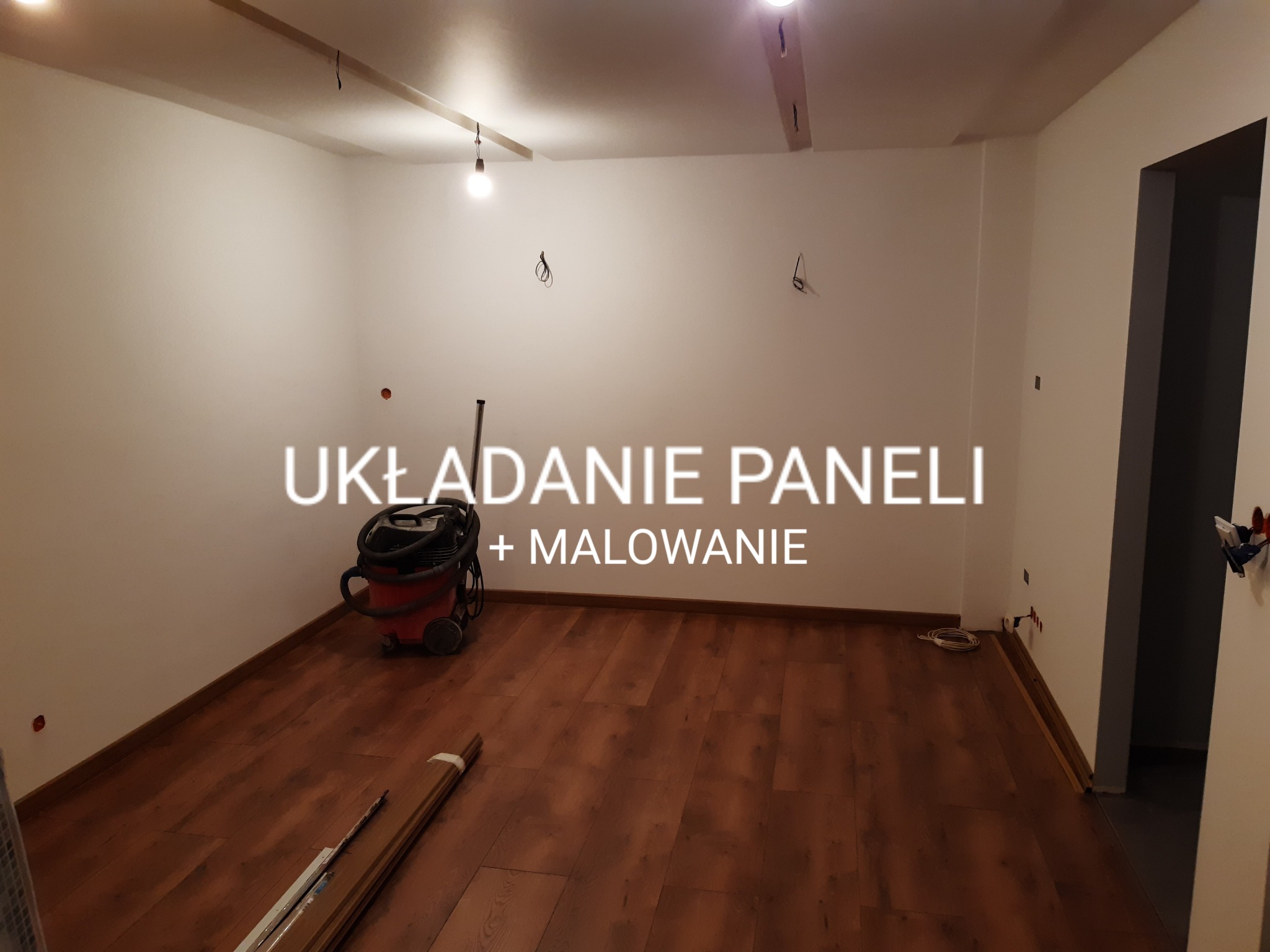 Pokój w trakcie remontu: świeżo ułożone panele podłogowe w odcieniach brązu, ściany pomalowane na biało, widoczny odkurzacz przemysłowy i listwy przypodłogowe przed montażem.