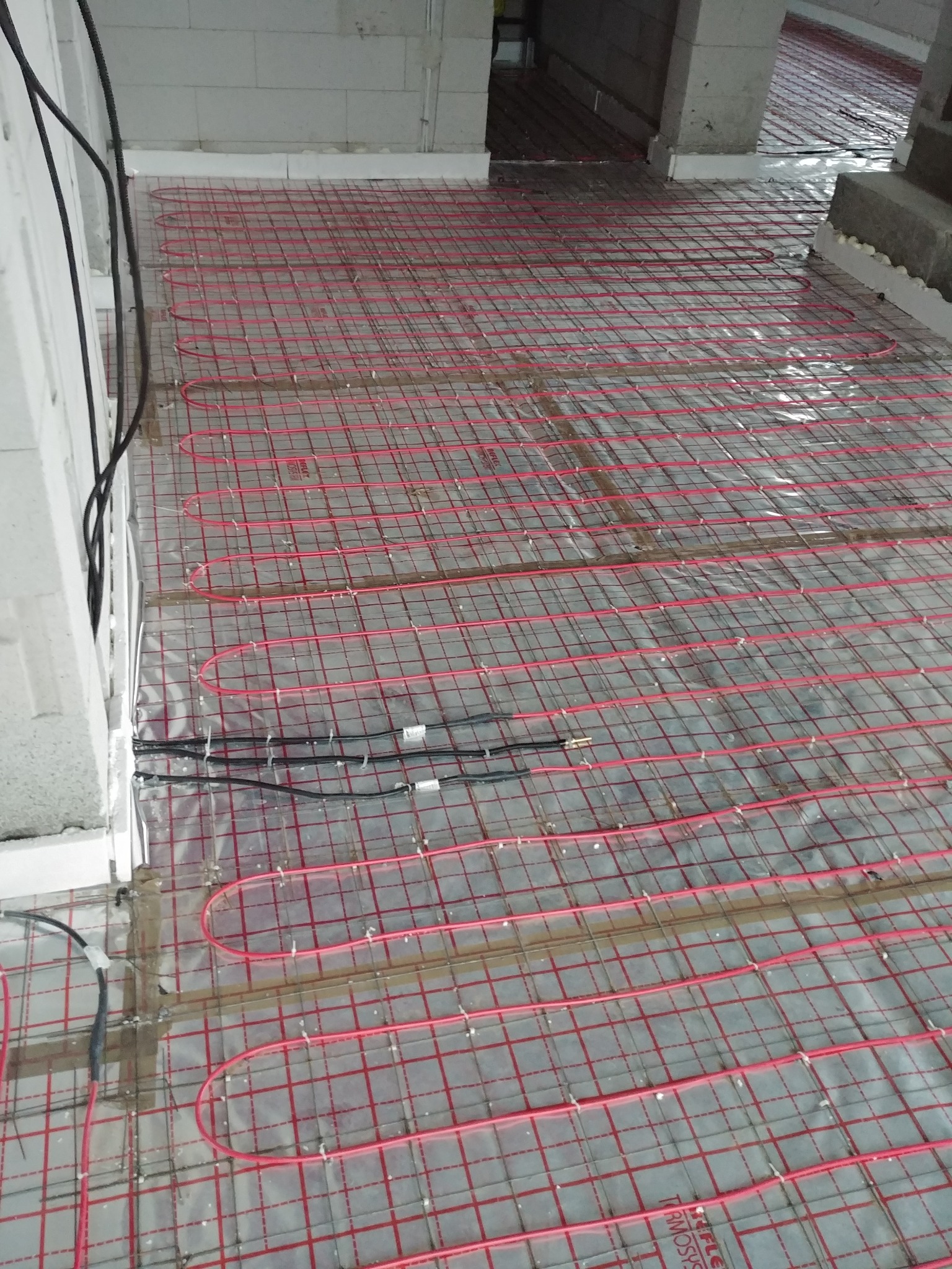 Montaż ogrzewania podłogowego w Nowej Wsi Wielkiej, widoczne czerwone rurki układane na metalowej siatce w surowym stanie, przed wylewką.