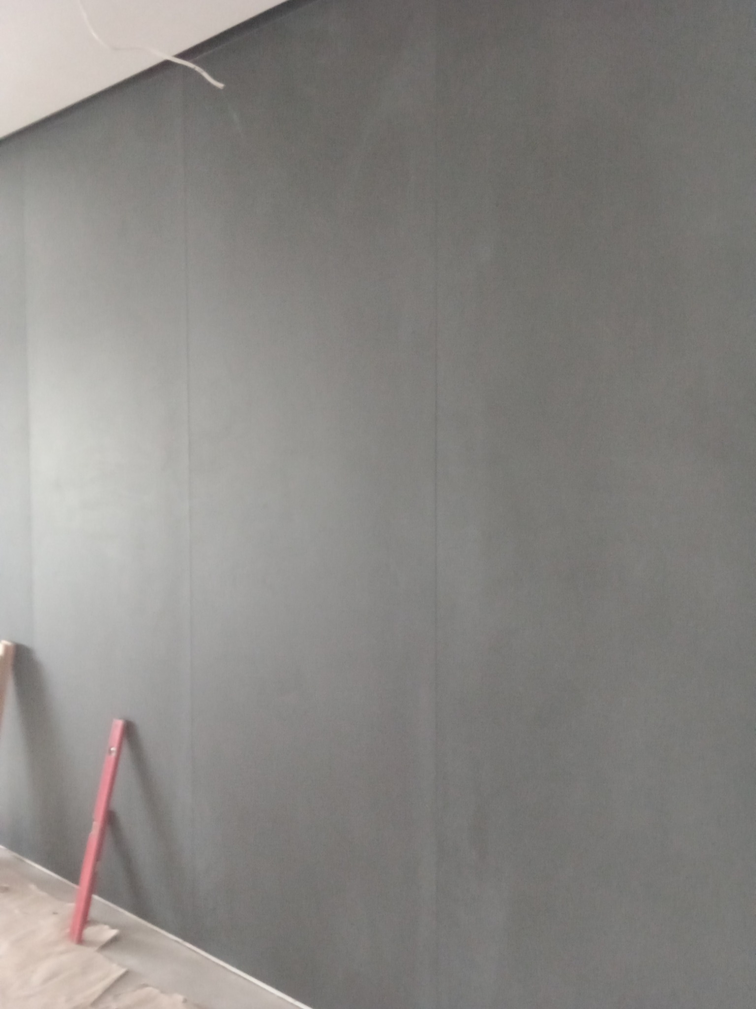 Świeżo położona, ciemnoszara ściana z widocznym poziomem w rogu, sugerująca prace wykończeniowe w trakcie.