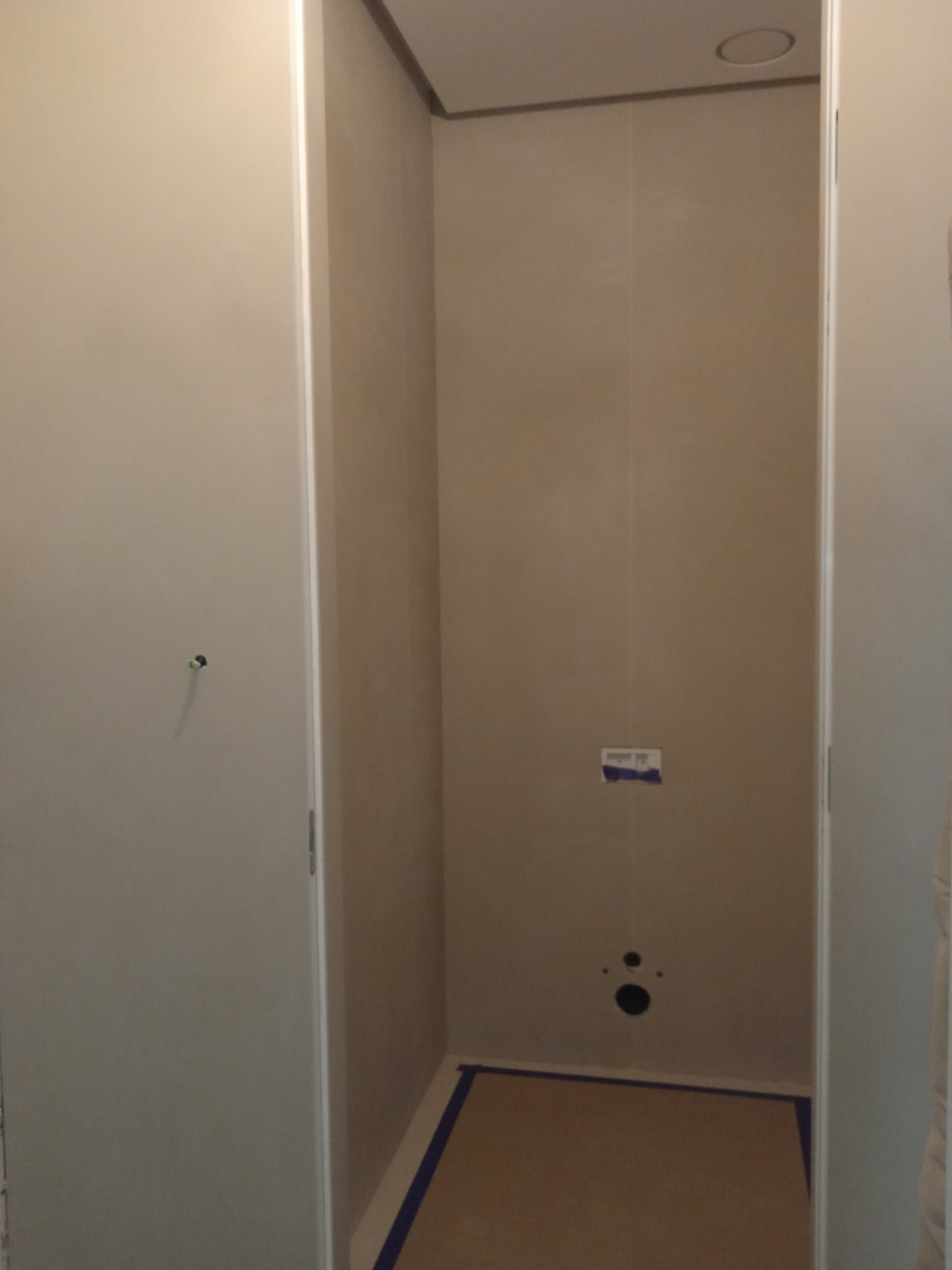 Surowe wnętrze łazienki w trakcie przygotowania do prac wykończeniowych, widoczne otwory na instalacje, zabezpieczona podłoga, ściany przygotowane pod okładziny.