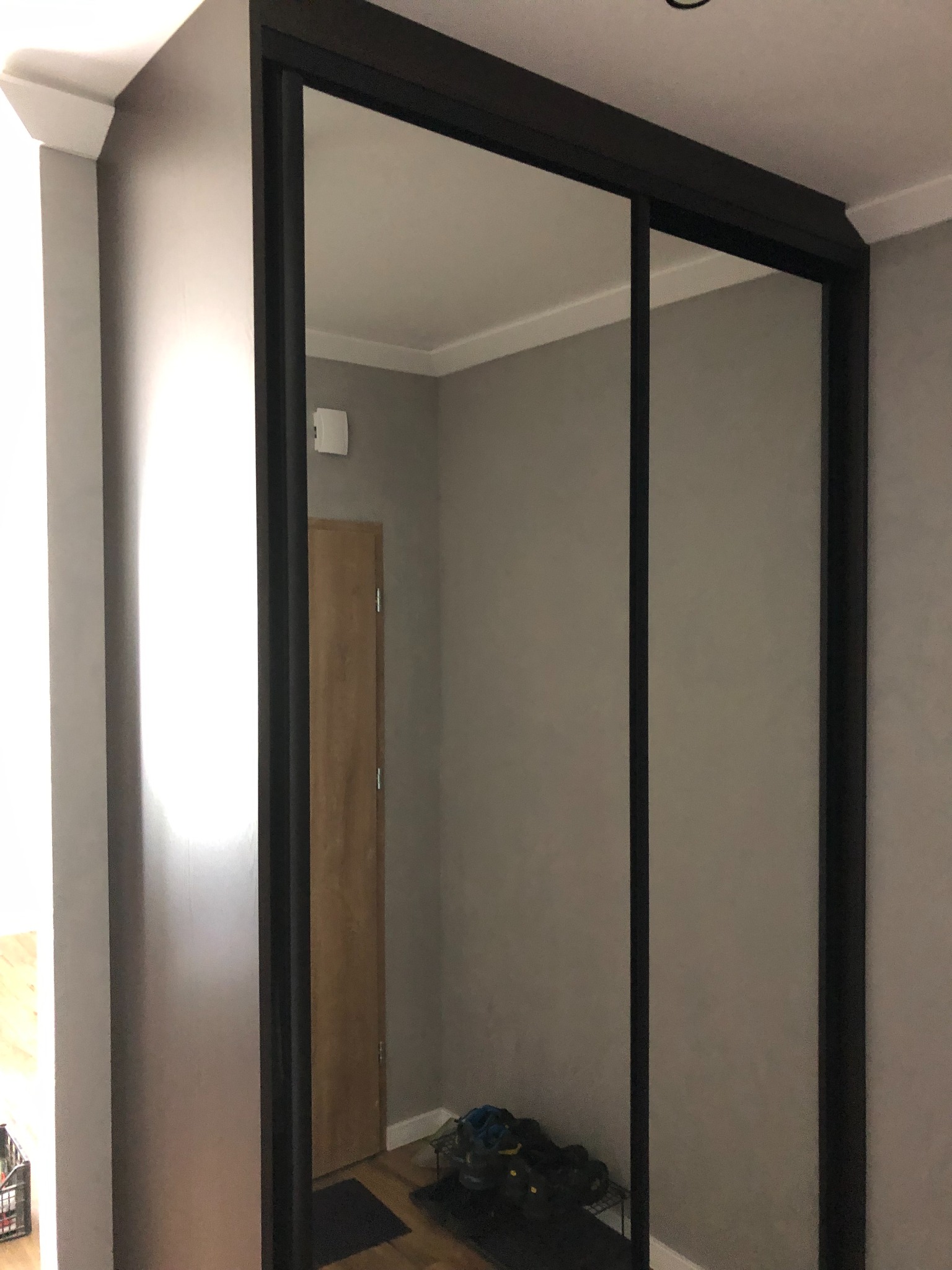 Nowoczesna szafa wnękowa z przesuwnymi drzwiami lustrzanymi w Augustowie, z ciemną ramą i widoczną podłogą oraz obuwiem wewnątrz.