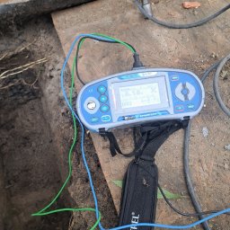 USŁUGI INSTALACYJNE PAWLED - Miernik Metrel z sondami w ziemi, pokazujący wynik pomiaru. Przewody w kolorach: niebieski, zielony. Pomiar rezystancji uziomu.