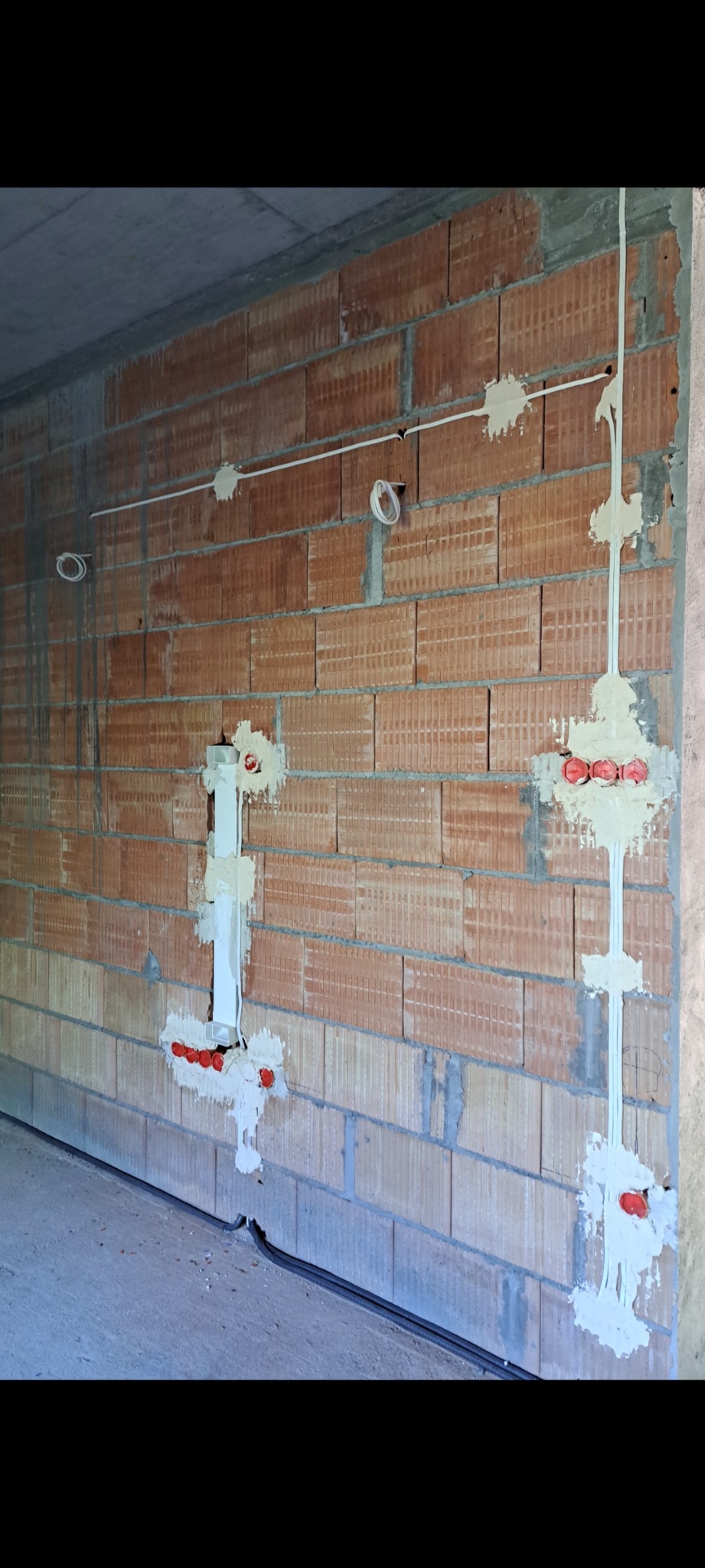 Instalacja elektryczna w trakcie montażu na ceglanej ścianie. Widoczne przewody, puszki i mocowania. Prace instalacyjne w surowym wnętrzu.