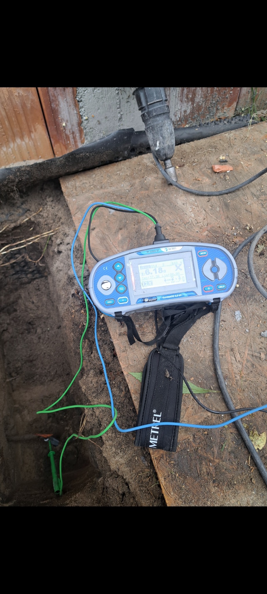 Miernik Metrel z sondami w ziemi, pokazujący wynik pomiaru. Przewody w kolorach: niebieski, zielony. Pomiar rezystancji uziomu.