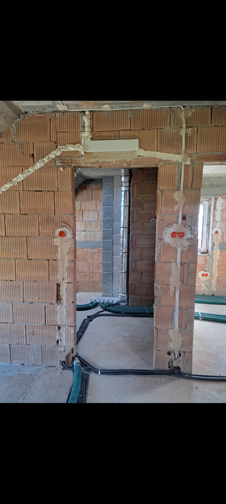 Wnętrze w trakcie prac: widoczne kable elektryczne w peszlach ułożone na podłodze, puszki instalacyjne w ścianach z cegły dziurawki, piony wentylacyjne.