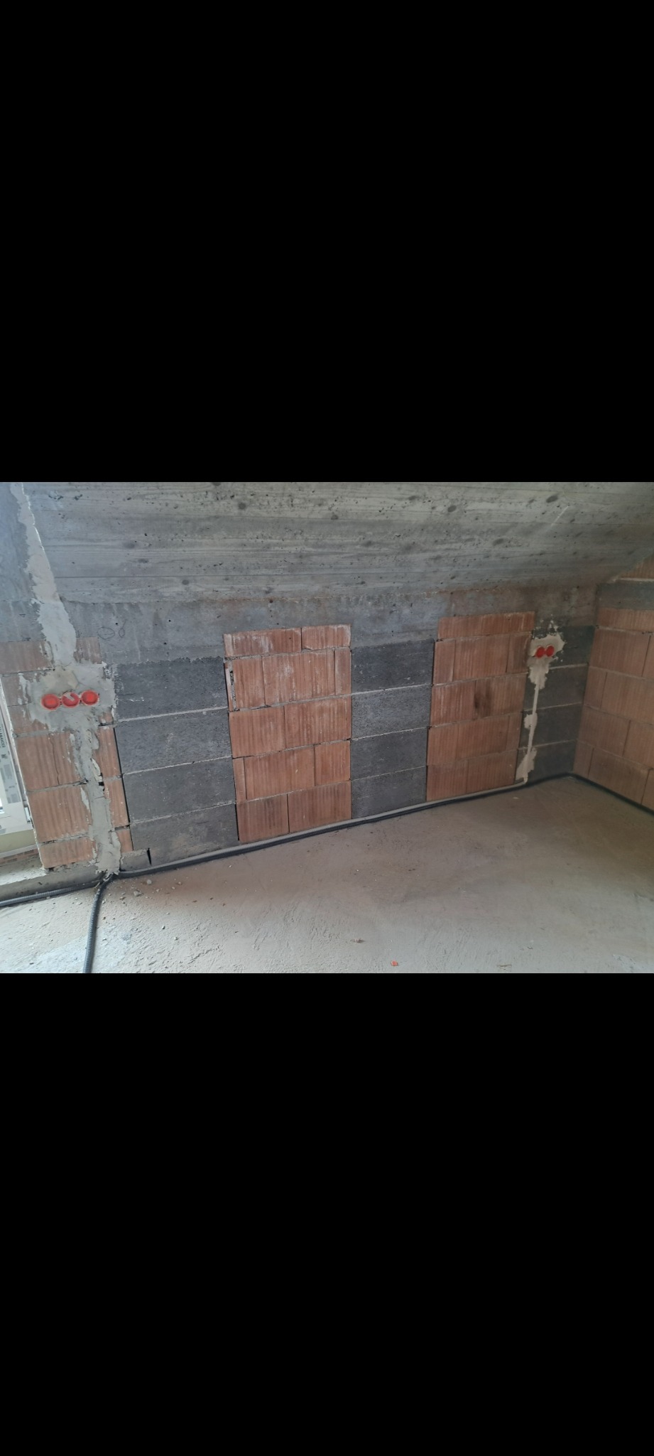 Wnętrze w trakcie prac: widoczne przewody elektryczne w peszlach ułożone wzdłuż ściany z pustaków, puszki instalacyjne w ścianach. Stan surowy.