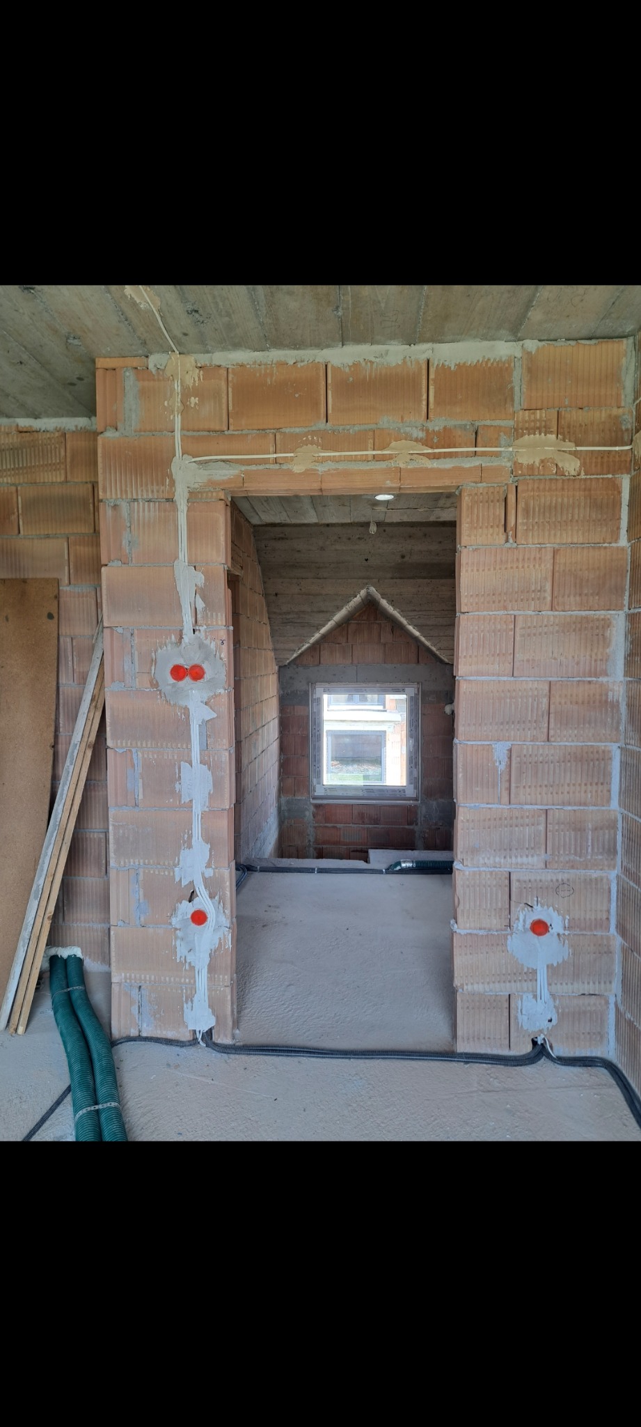 Wnętrze w trakcie budowy z widoczną instalacją elektryczną w ścianach z czerwonej cegły. Kable prowadzone w bruzdach, puszki elektryczne zamontowane. Surowy stan.