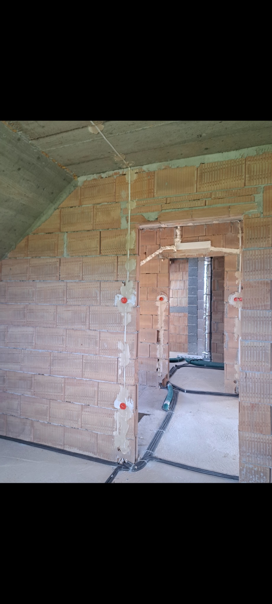 Surowy stan: kable elektryczne i puszki w ścianach z cegły dziurawki, brak tynków. Widoczne przewody na podłodze prowadzone wzdłuż ścian.