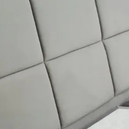 Szary, tapicerowany zagłówek łóżka z geometrycznym wzorem kwadratów, widoczny fragment materaca.