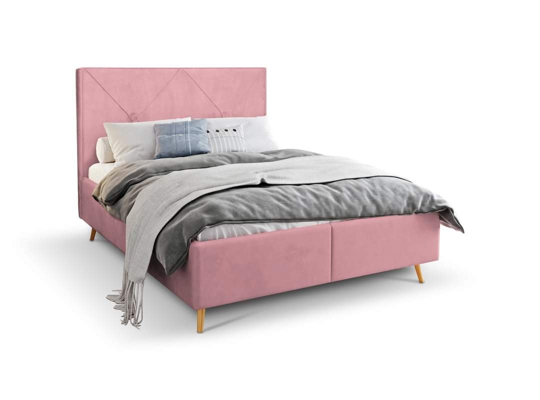 Różowe łóżko tapicerowane z pikowanym wezgłowiem, drewnianymi nóżkami i szarym pledem na białym tle.