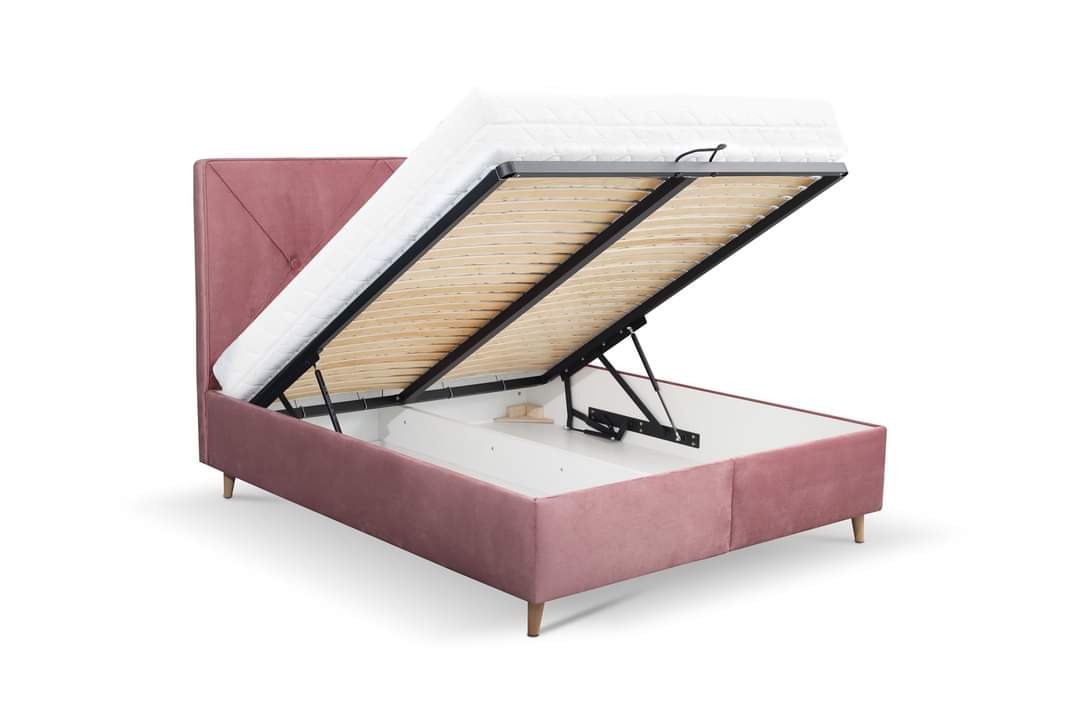 Różowe tapicerowane łóżko z podnoszonym stelażem i widocznym pojemnikiem na pościel, materac uniesiony do góry.