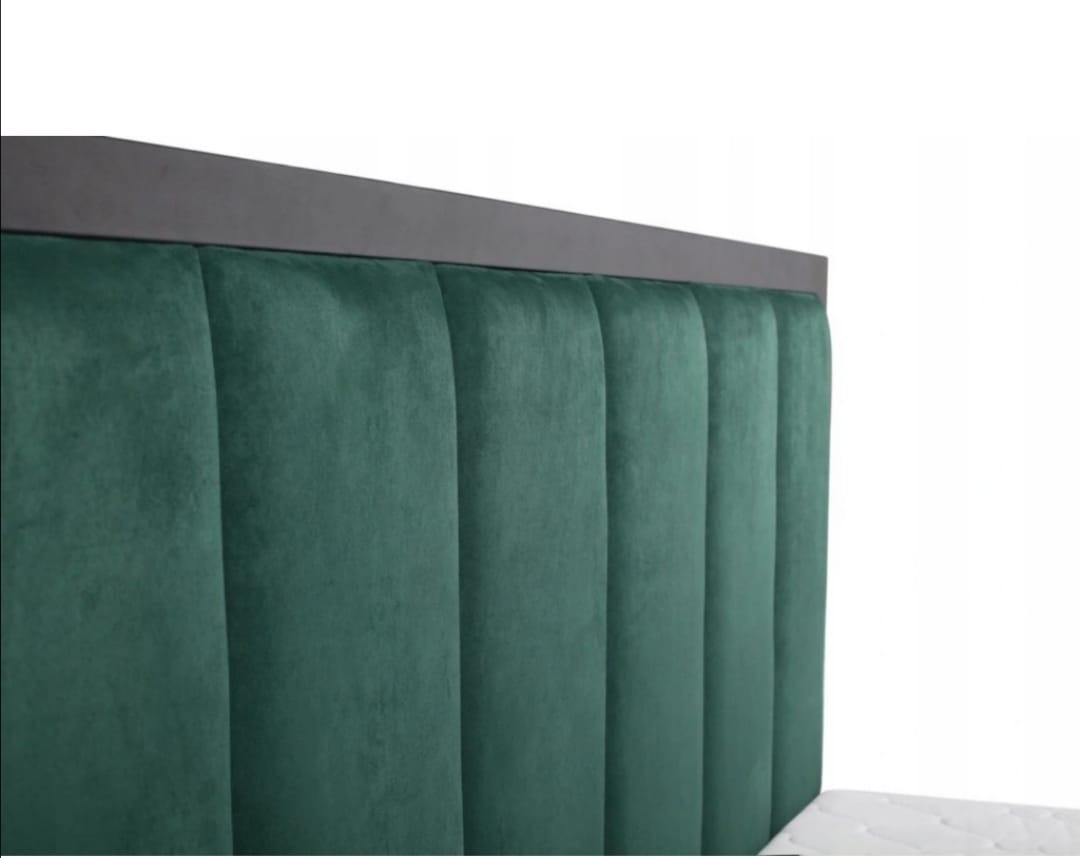 Fragment wezgłowia łóżka z ciemnozieloną, pionowo pikowaną tapicerką welurową i ciemnoszarą ramą.