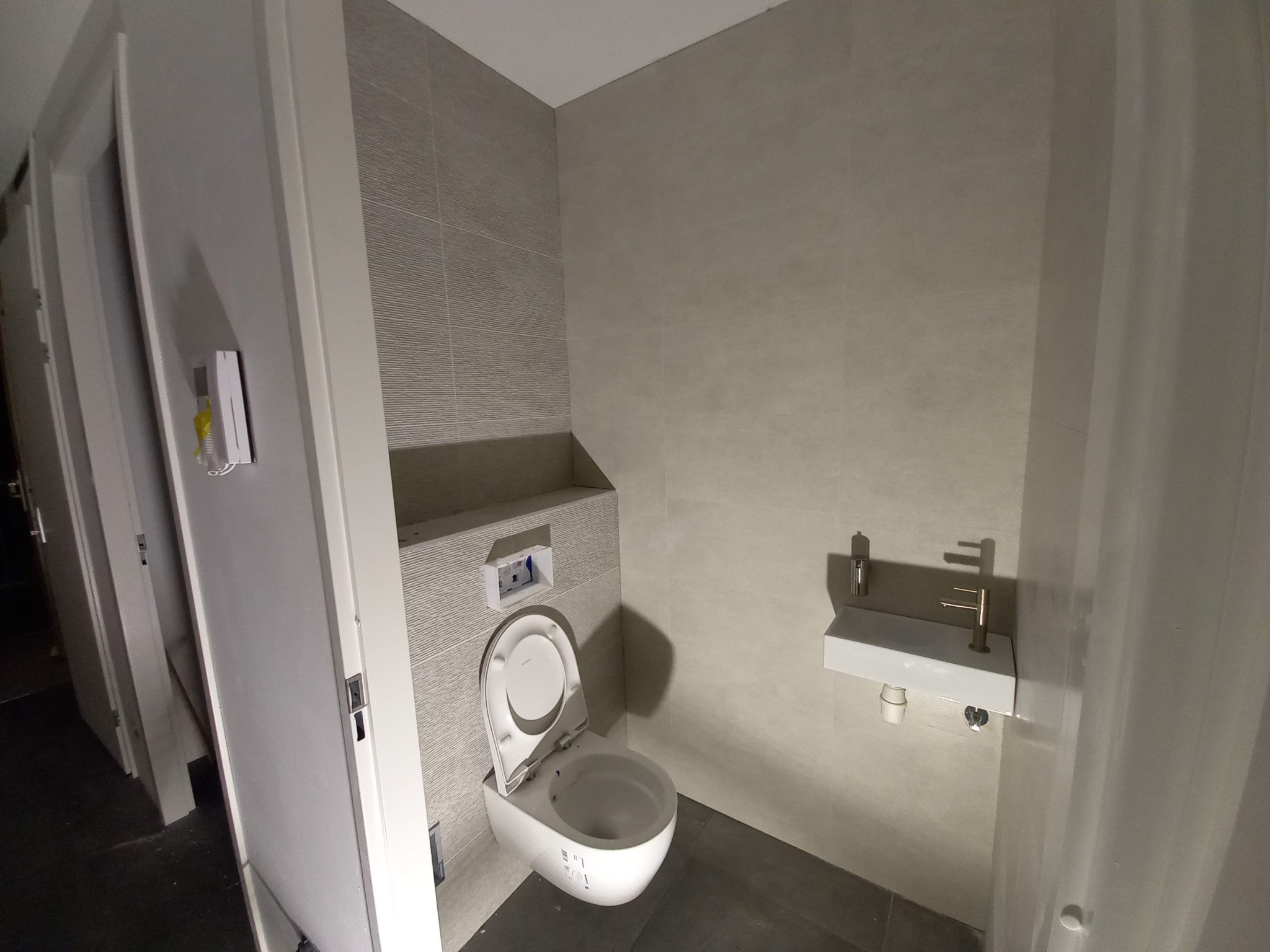 Nowoczesna łazienka z podwieszaną toaletą, minimalistyczną umywalką i szarymi płytkami imitującymi fale.