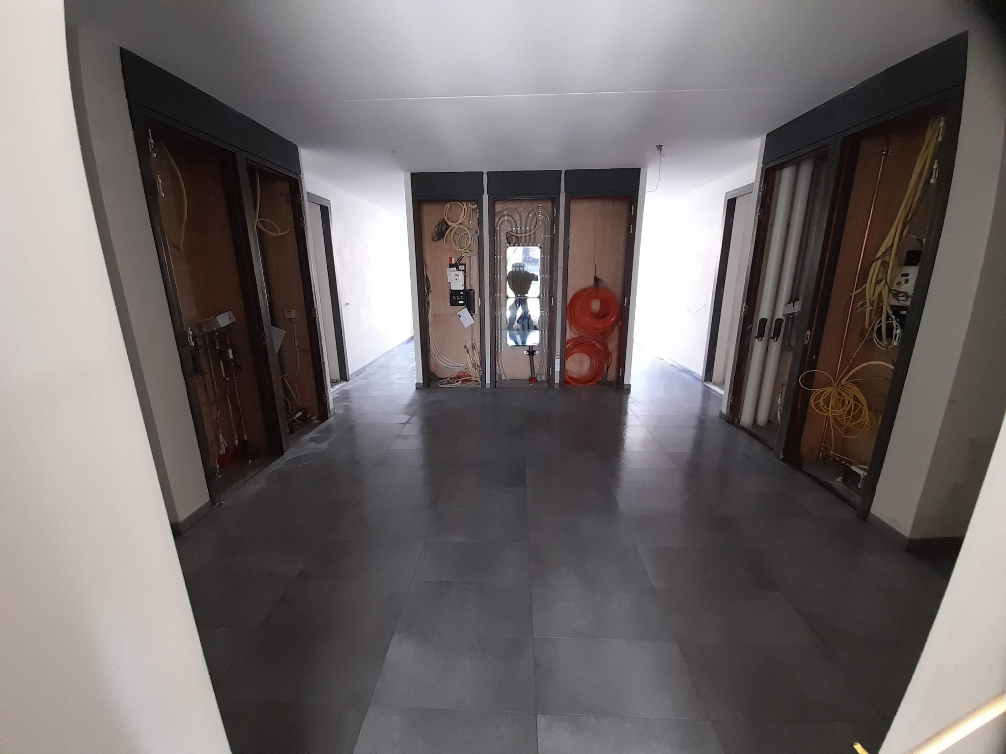 Korytarz w trakcie remontu z widocznymi instalacjami elektrycznymi i hydraulicznymi w ścianach, przygotowany do układania płytek na podłodze.