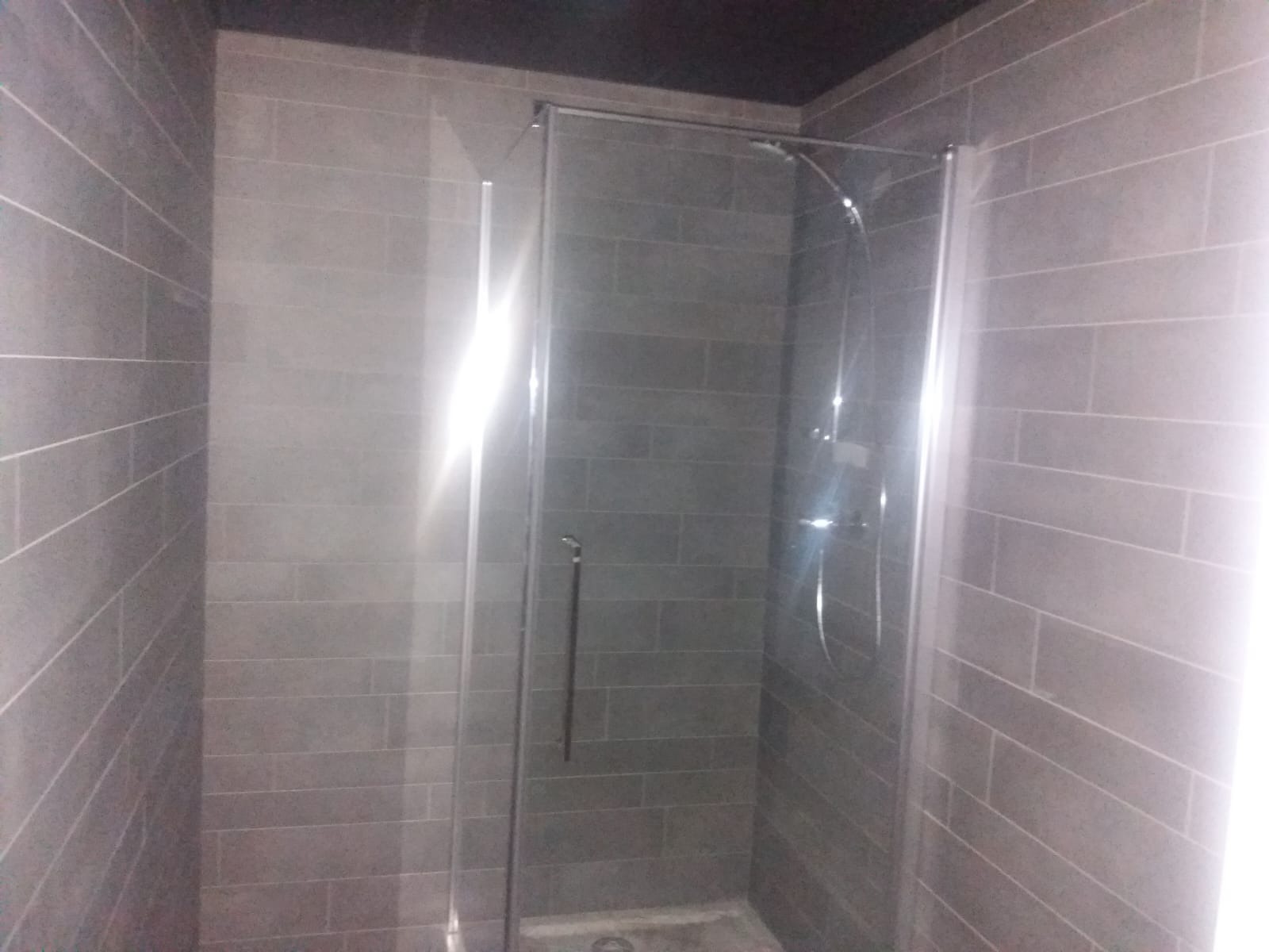 Wykończona kabina prysznicowa z szarymi, podłużnymi płytkami imitującymi cegłę, chromowana armatura, widoczne fugi.