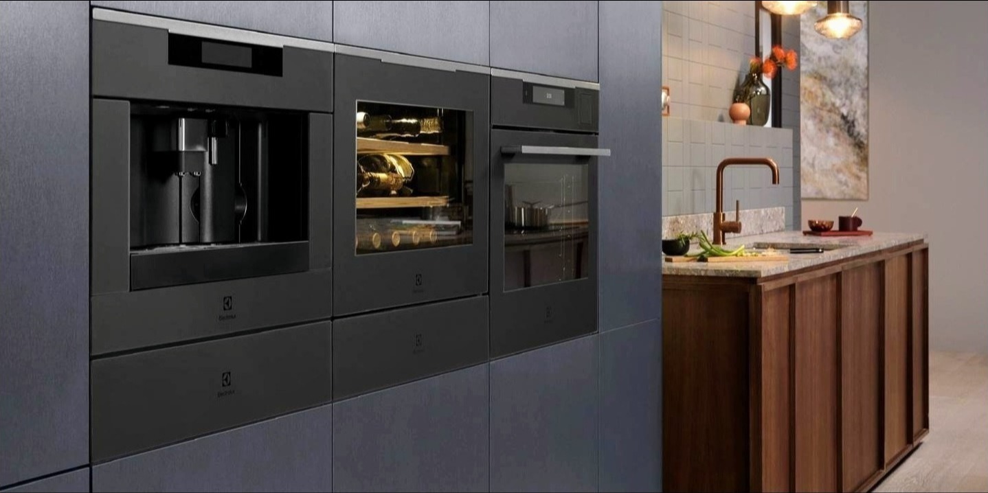 Wbudowana zabudowa kuchenna z czarnymi urządzeniami Electrolux: ekspres do kawy, chłodziarka do wina z oświetleniem LED i piekarnik. Miedziana bateria kuchenna na blacie z granitu.