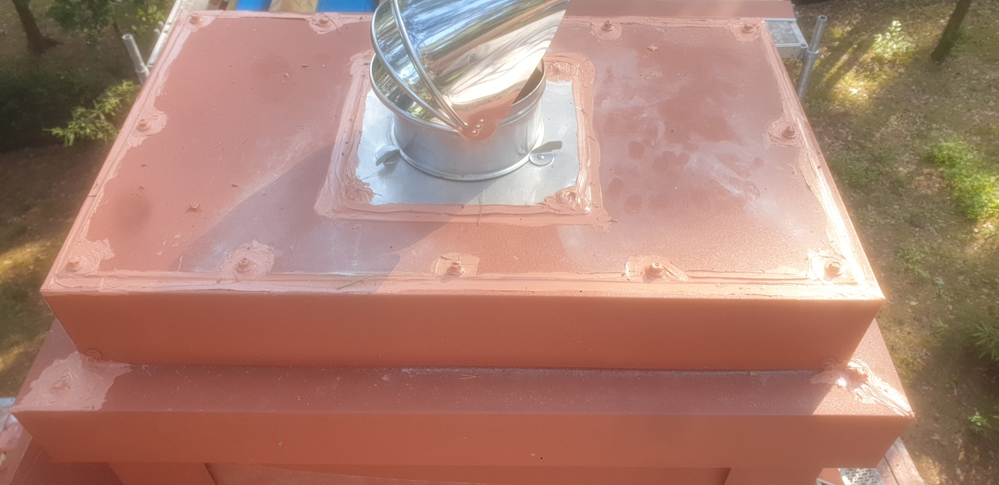 Wykończony komin z metalowym wkładem, zabezpieczony silikonem, pomalowany na ceglasty kolor, widok z góry.