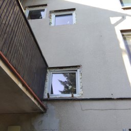 Jarmarhome - Montaż okien w elewacji budynku z widocznymi szczelinami wypełnionymi pianką montażową i częściowo usuniętym starym tynkiem.