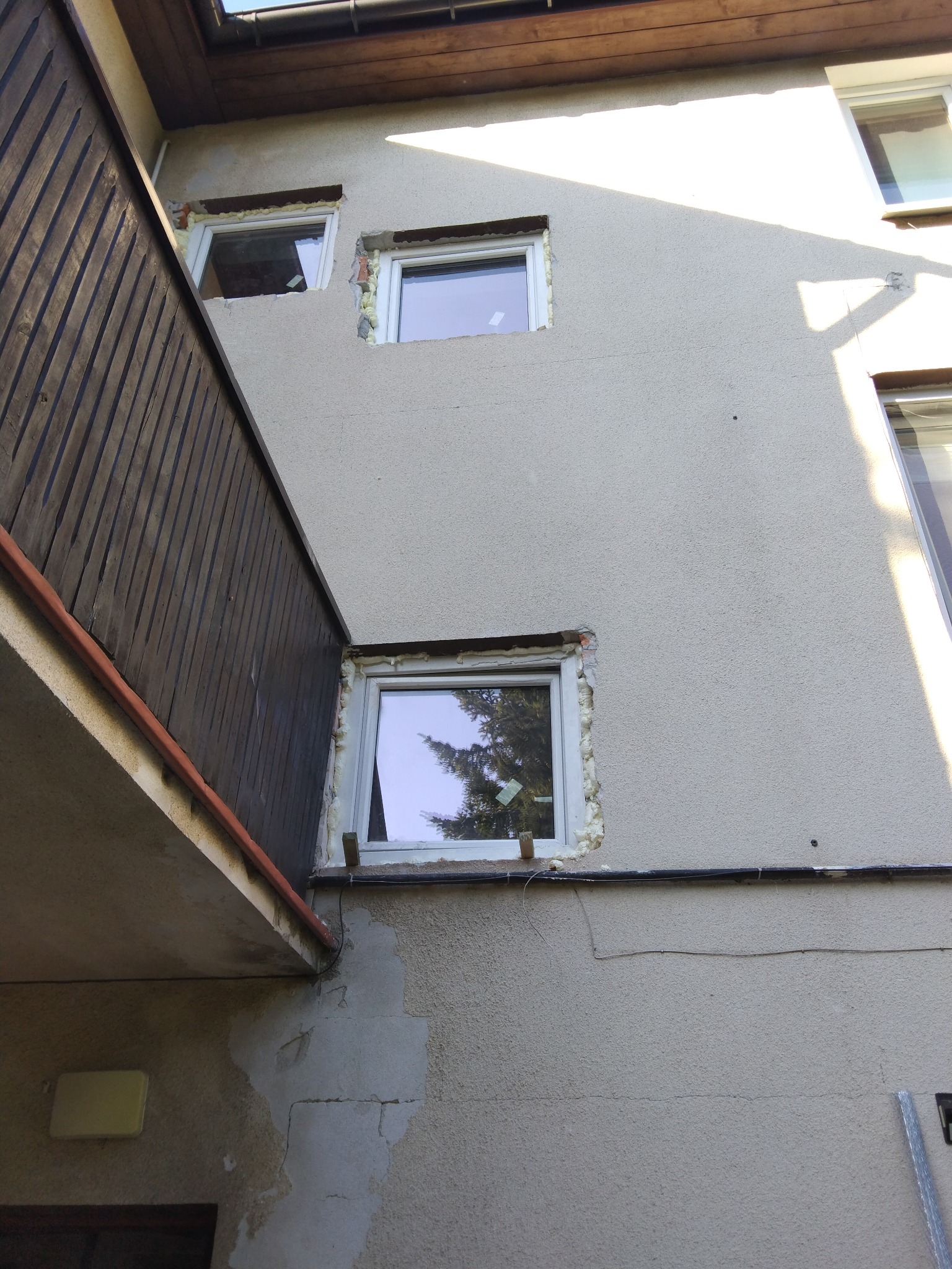 Montaż okien w elewacji budynku z widocznymi szczelinami wypełnionymi pianką montażową i częściowo usuniętym starym tynkiem.