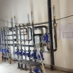 Instalacja przemysłowa z rur i zaworów w piwnicy, widoczne elementy montażowe, plan instalacji na ścianie i narzędzie do obróbki rur