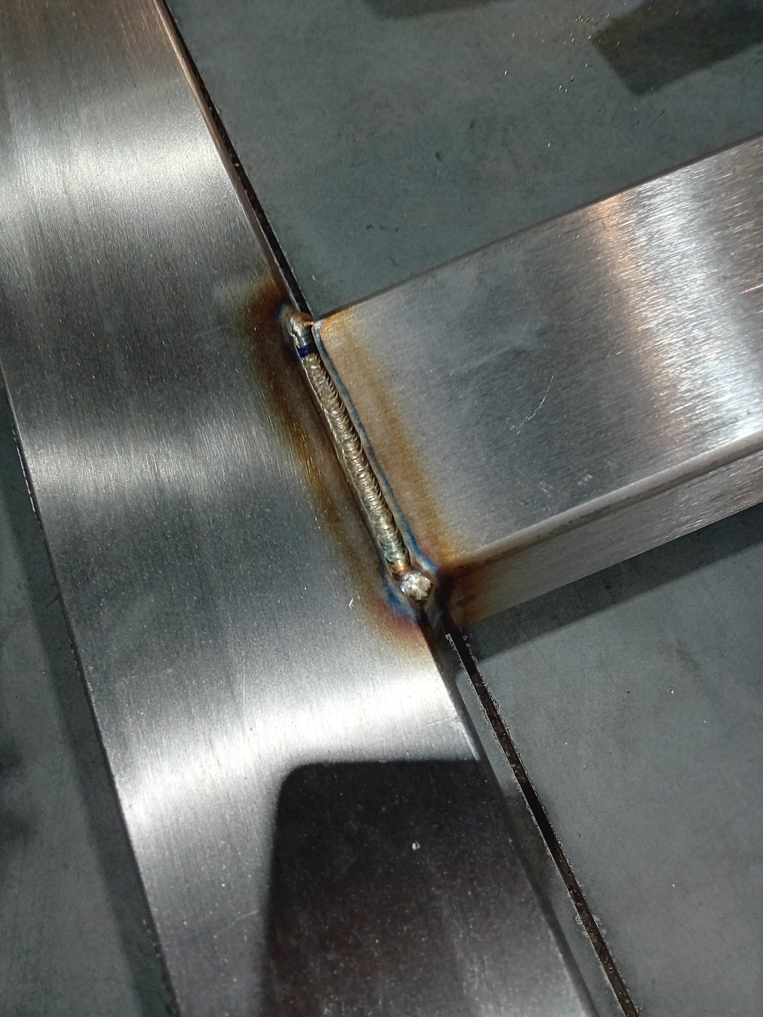 Spoina łącząca metalowe elementy pod kątem prostym, widoczne ślady przypaleń i nierówności spoiny.