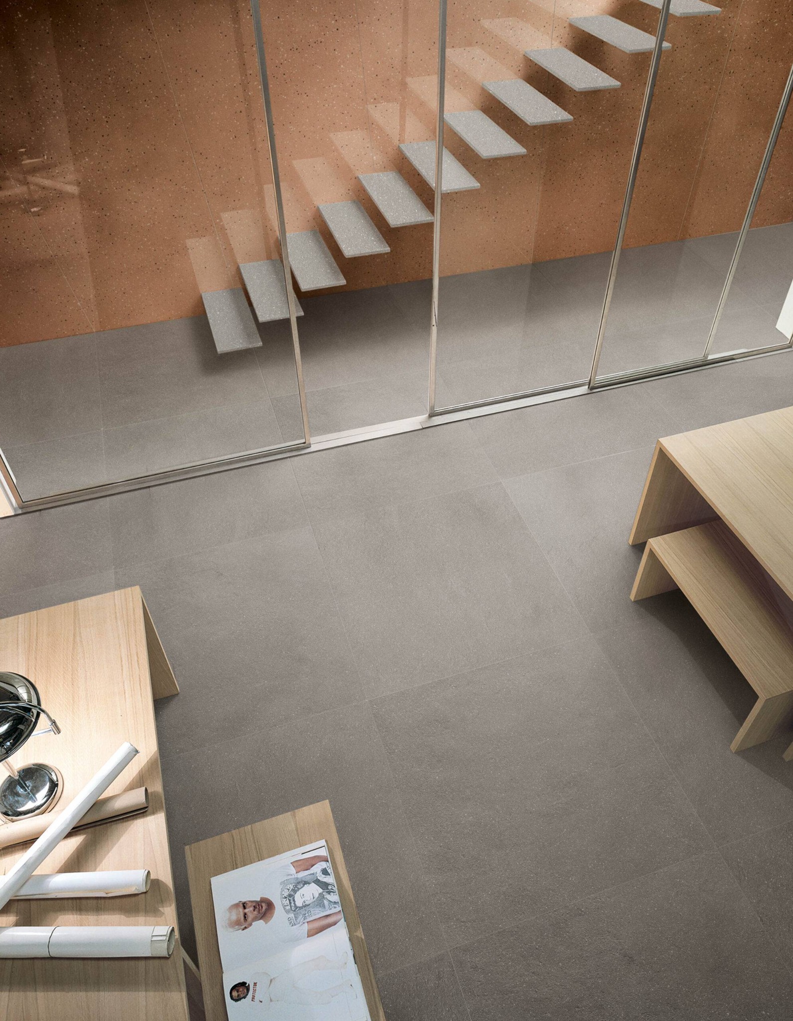 Minimalistyczne wnętrze z szarymi płytkami podłogowymi, oranżową ścianą z drobnym wzorem, szklaną ścianą i schodami oraz drewnianymi stolikami kawowymi z magazynem i zwiniętymi planami