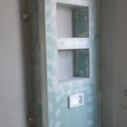 Ściana z płyty kartonowo-gipsowej z wnękami, wstępnie zagruntowana, widoczne instalacje hydrauliczne w dolnej części ściany.